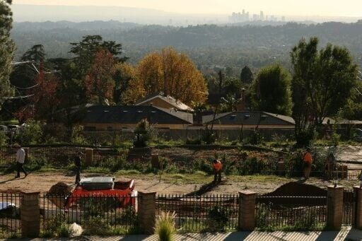 Workers dig the foundations of a house in Altadena, with the towers of downtown Los Angeles visible in the distance