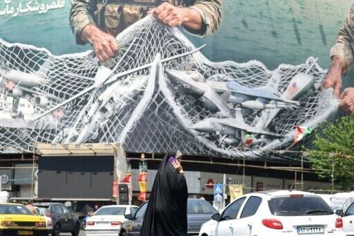 A woman walks past a giant billboard in Tehran that reads 'the Strait of Hormuz remains closed.'