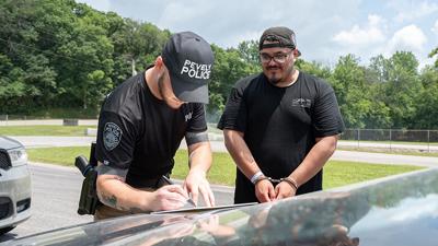 Officer Christopher Jones of Pevely Police writes a fake citation for Christian Lopez as he waits in handcuffs.