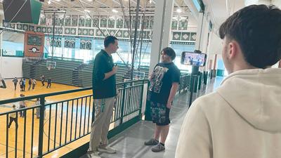 Camera operator Eli Edgar, a senior, watches Kris Pyrtle, a senior, practice interviewing his instructor, Julius Rotter, about the new video board in the high school gym.