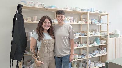 From left, Chelse and Kelsey Schleusner stand in front of glazed pottery pieces in their studio, Ember & Earth.