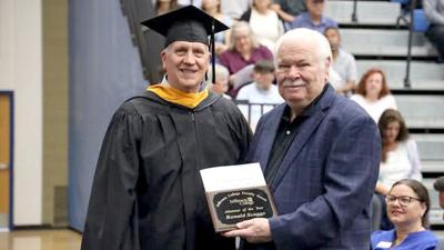 Board of Trustees member Steve Meinberg presents Ron Scaggs with Alumnus of the Year at the 2026 commencement.
