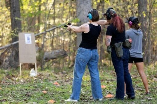 A student (L) prepares to shoot as Clara Elliott (C) instructs proper technique during an introductory firearms class near Richmond, Virginia