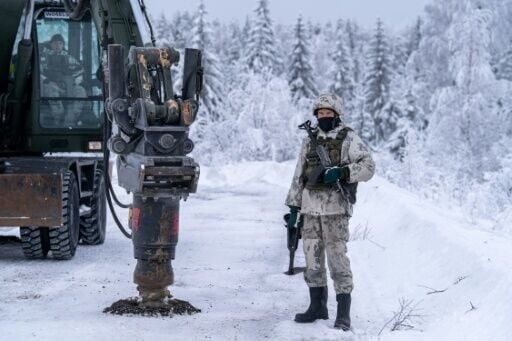 The military uses an excavator to dig into the frozen asphalt to bury anti-tank mines