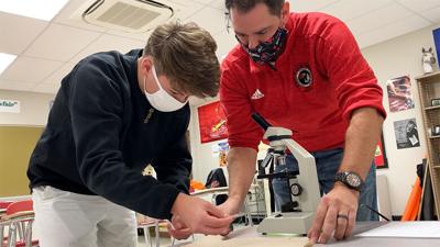 Fox High School teacher Jeremy Conley helps a student set up a microscope.