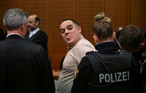 A co-defendant, Ukrainian Robert A., sticks out his tongue as he is led into the courtroom