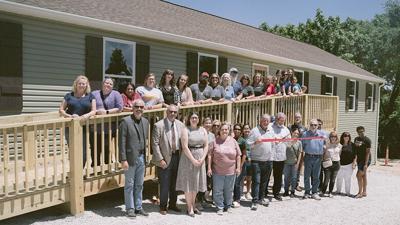 Members of the community join Dan Ross Jr., center, holding scissors, in a ribbon- cutting ceremony on May 29 for Cedar Oak, a sober living facility in Peaceful Village.