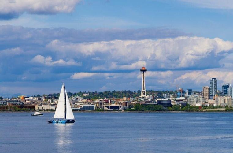 a sailboat moves in front of the space needle as viewed from a ferry in the puget sound