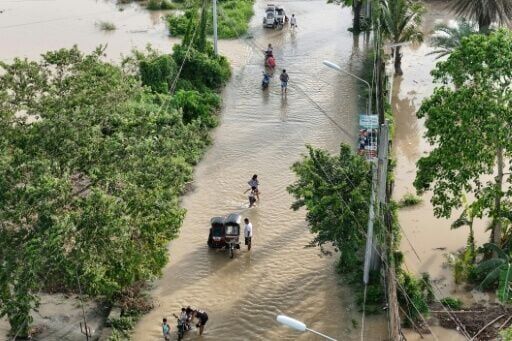 People wade through the water along a submerged street in Tuguegarao City in the Philippines' Cagayan province