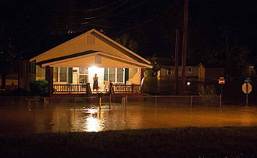 A De Soto resident on the porch at 815 Dewitt talks on the phone as floodwaters surround the house.