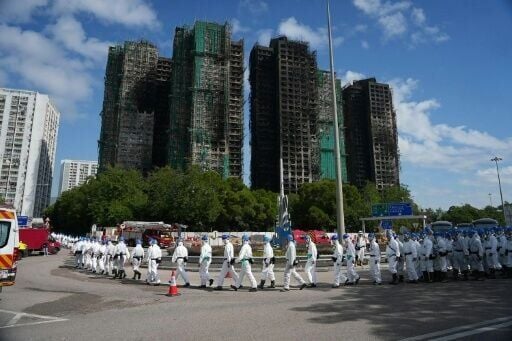 Police officers from the Disaster Victim Identification Unit (DVIU), dressed in white-coloured full-body protective gear, walk past the housing blocks of Wang Fuk Court in the aftermath of the deadly November 26 fire