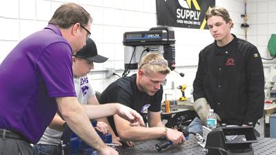 Industrial technology teacher Benjamin Ferrell, center, demonstrates how to use a virtual reality welding simulator.