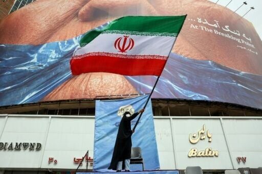 A woman waves an Iranian flag in front of an anti-US billboard referring at Valiasr Square in Tehran