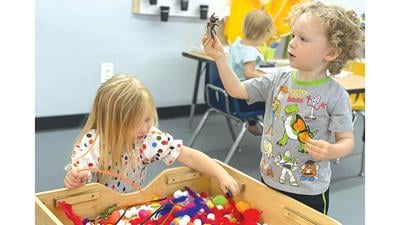 Asher Ahern, 2, looks intently at a fake bug while holding a butterfly in his other hand while Lydia Allemann, 3, helps him look for other bugs in the sensory bin.