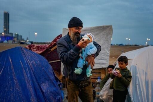 A man feeds his baby with a bottle at a make-shift camp for the displaced set up along the seafront in the Lebanese capital Beirut