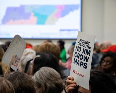 Protesters hold signs during a House committee meeting, May 6, 2026
