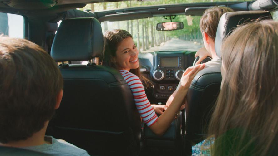 Rear View Of Family On Road Trip In Convertible Car Driving Along Tree Lined Road