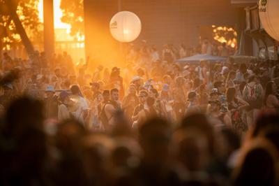Color photo of a large crowd during sunset at Bonnaroo 2024, with a man in a thoughtful pose almost like Rodin’s famous sculpture ‘The Thinker’ in the center
