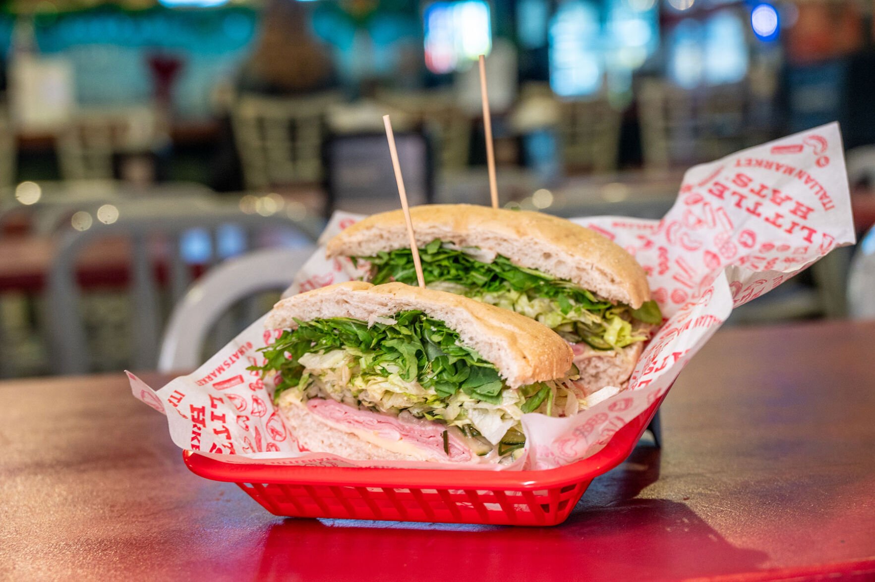 A ham and rosemary sandwich cut in half, skewered with toothpicks and nestled in a red basket