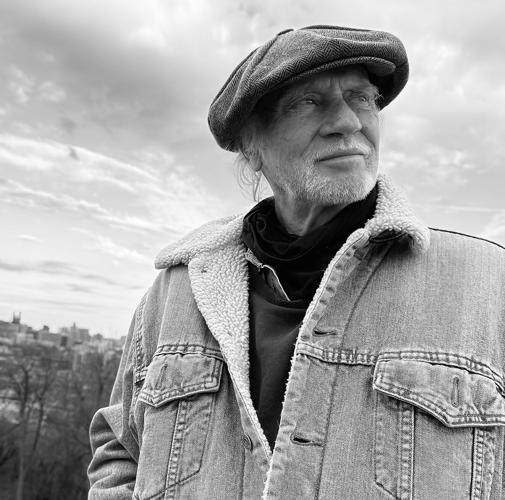 Black and white photo of Chris Gantry, outside in a winter coat open at the neck, wearing a drivers cap, with the Nashville skyline deep in the background.