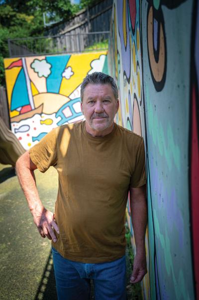 A man leans against a colorful mural outside Safe Haven Family Shelter