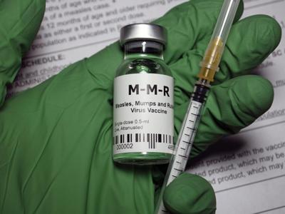 Green medical gloved hand holding a MMR vaccine vial