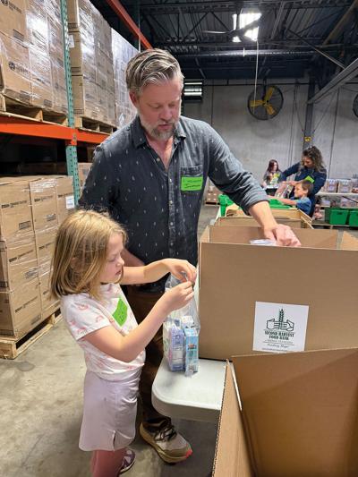 A man and a girl pack juice boxes into a bag next to a carboard box at Second Harvest, our Writer's Choice for Best Volunteer Opportunity for Kids (During the School Year).
