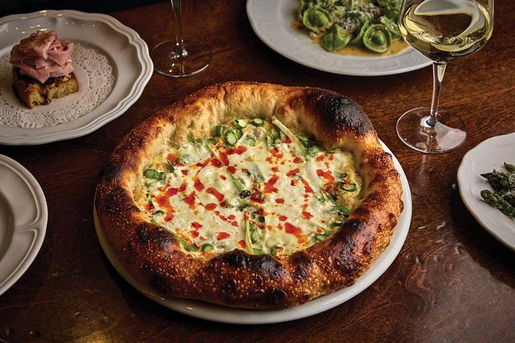 A pizza placed next to a glass of wine, pasta and piece of bread topped with meat