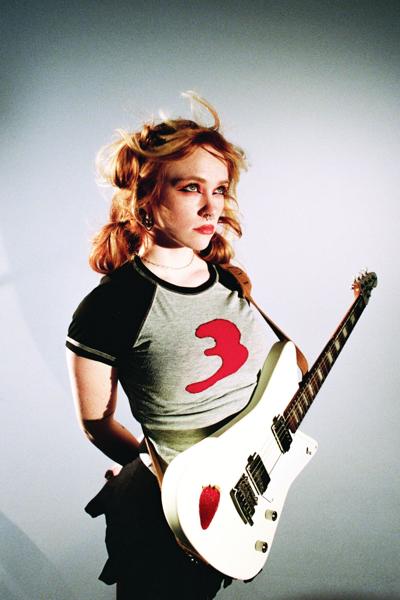 Studio color portrait of RobinAugust, standing with her white electric guitar strapped on