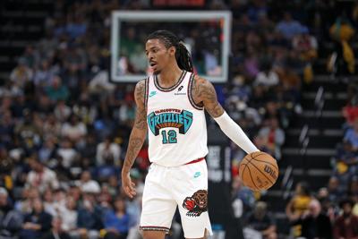 Ja Morant in a white jersey with a "Grizzlies" written in cerulean blue across the chest, the number 12 below it, holding a basketball in his left hand with a hoop in the distance.