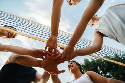 Stock photograph shot from below a volleyball team putting their hands into the middle of a circle to cheer at the start of a game