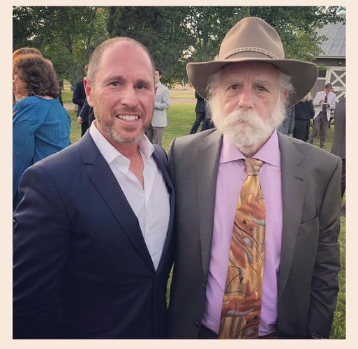Artist manager Jonathan Levine, wearing a blue suit jacket and a white Oxford shirt, stands with his friend and client, Grateful Dead co-founder Bob Weir. Weir has a bushy white beard and wears a gray suit with a brown cowboy hat, a pink Oxford shirt and a necktie that looks like it could be one of the ones based on paintings by Jerry Garcia.
