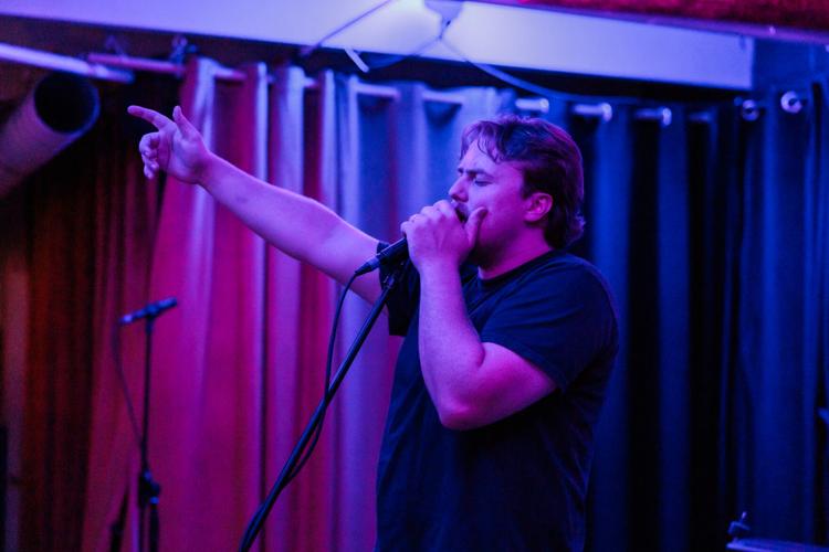 Paul Jesse singing into a microphone onstage at drkmttr