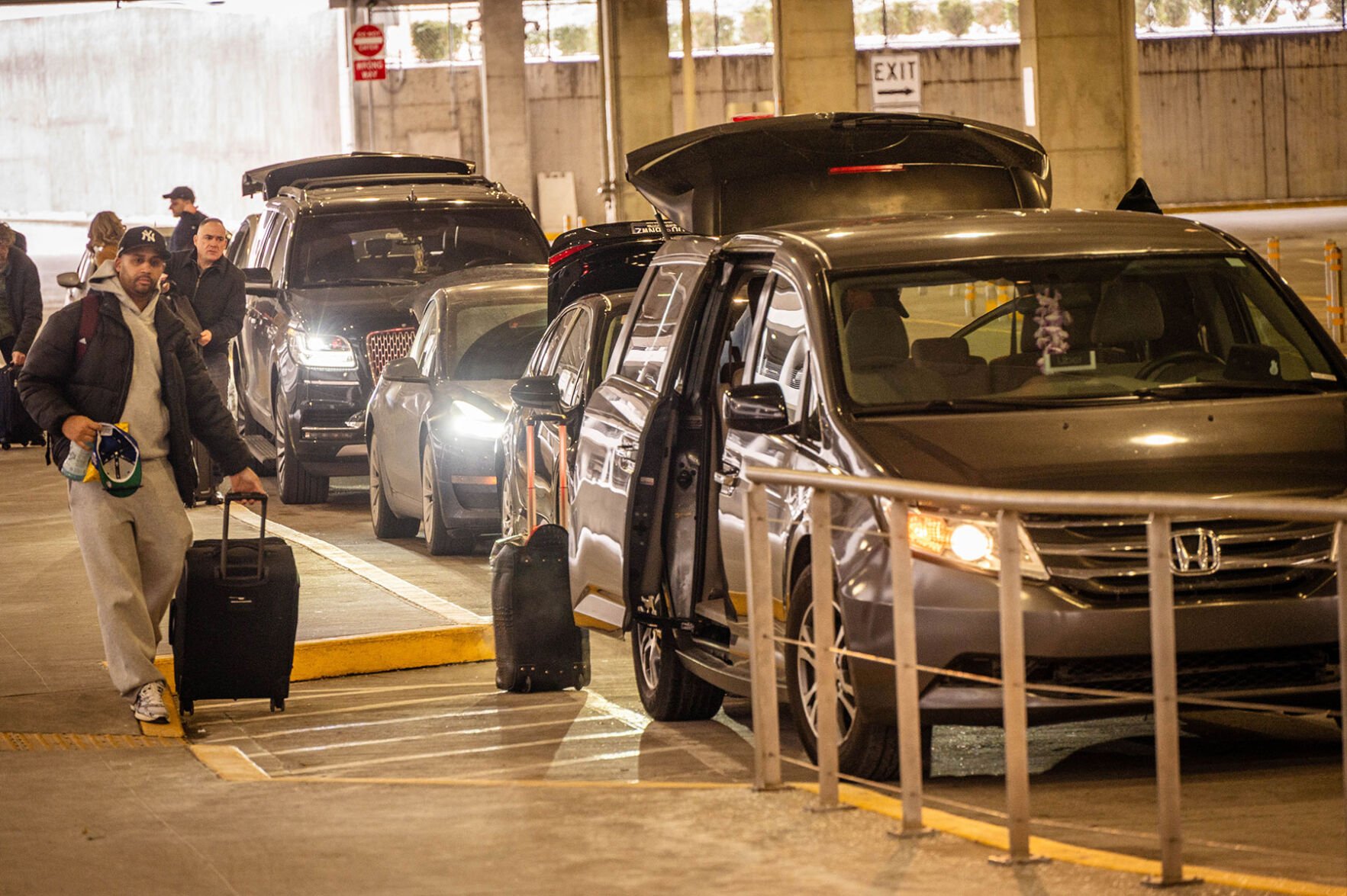 A row of cars with doors and trunks open at an airport parking garage