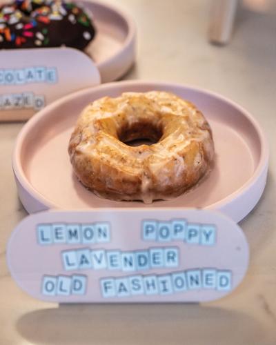 A doughnut on a pink plate with a sign reading "lemon poppy lavender old fashioned"