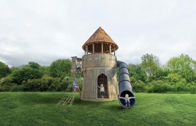 Children play at a wooden tower with a tall slide