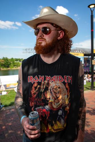 Color street style photograph of CMA Fest fan TJ Agnew, sporting a sleeveless Iron Maiden T-shirt and a cowboy hat.