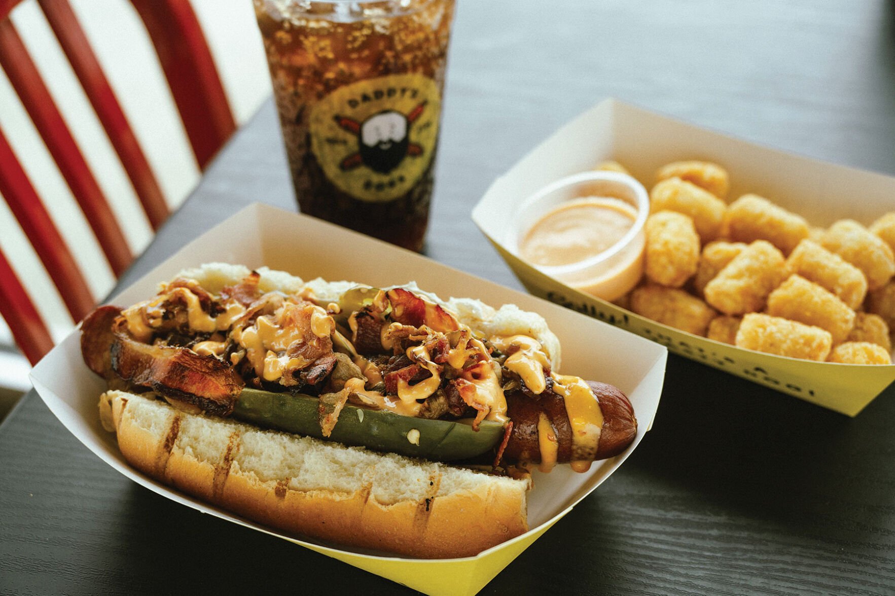 A loaded hot dog and tater tots with a soda