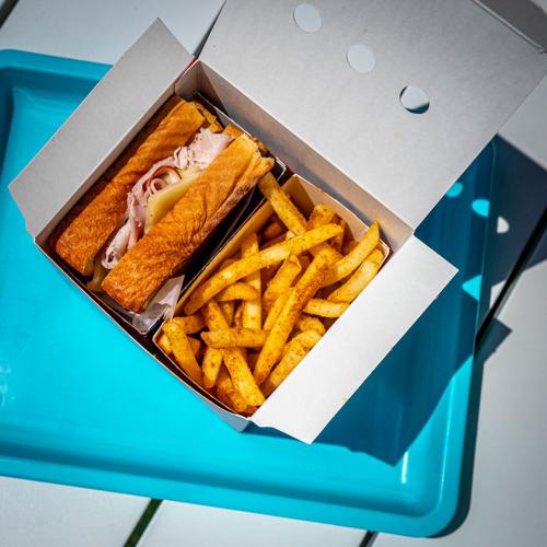 A ham and Swiss sandwich with fries in a takeout box