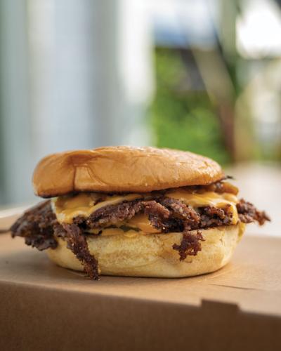 A crusty smashburger ona a flattened potato bun, charred beef and cheese pouring over the edges