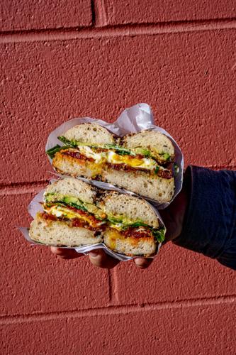 A hand holding up a bagel sandwich split in half, showing off the egg, bacon and lettuce