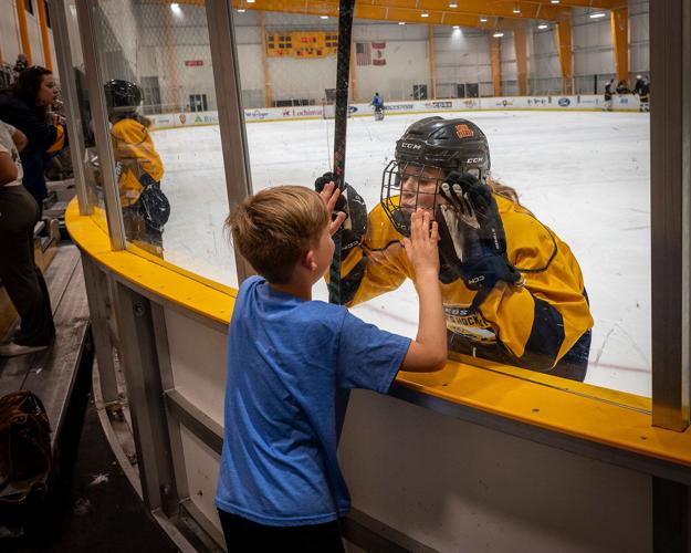 A woman dressed in hockey gear blows a kiss to a child from inside the Ford Ice Bellevue rink
