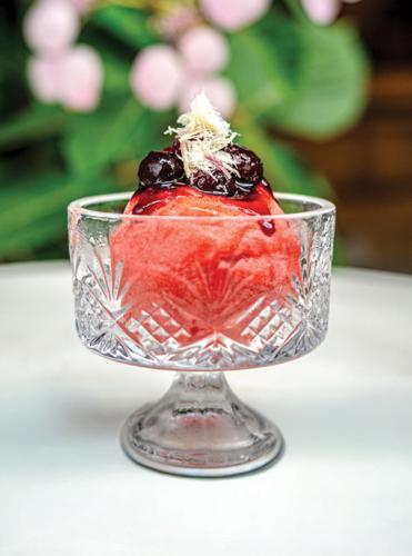 A short glass goblet with a bright pink scoop of sorbet topped with berries