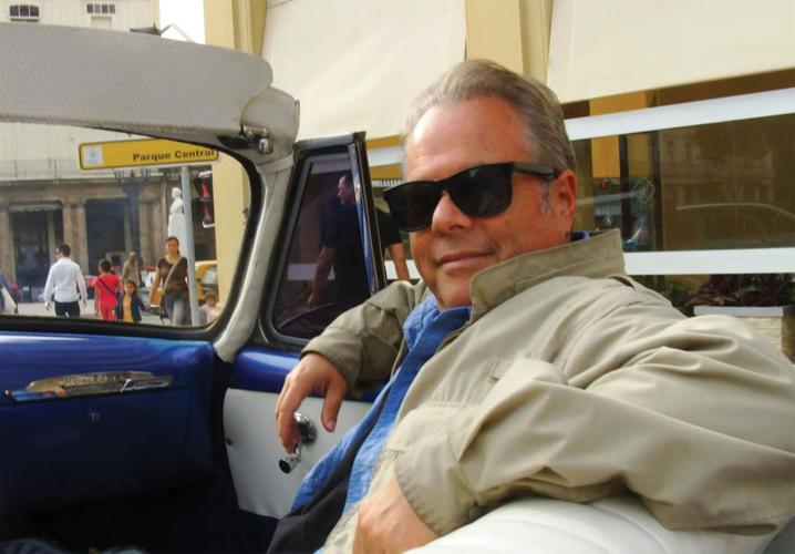 Stacy Widelitz wearing sunglasses in the passenger seat of a classic convertible car