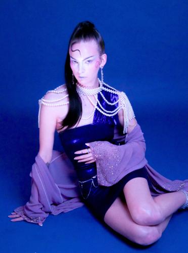 Color photo of musician Eve Maret, dressed in a black leather gown and a gray fabric wrap with an elaborate pearl necklace