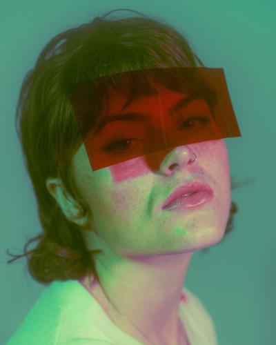 Molly Martin press photo artist wears a red lighting gel over her eyes