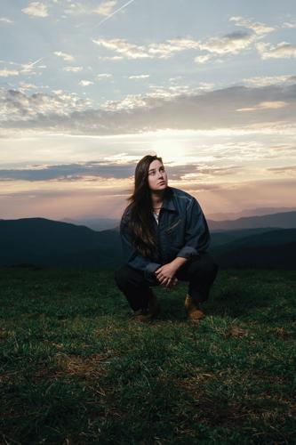 Color photo of Katie Pruitt in a field with her back to a sunrise or sunset, looking past the camera at audience-perspective right.