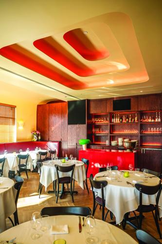 The interior of Junior with tables clad in white tablecloths, a yellow roof with rectangular recessions and a wall of bottles and glasses in the back.