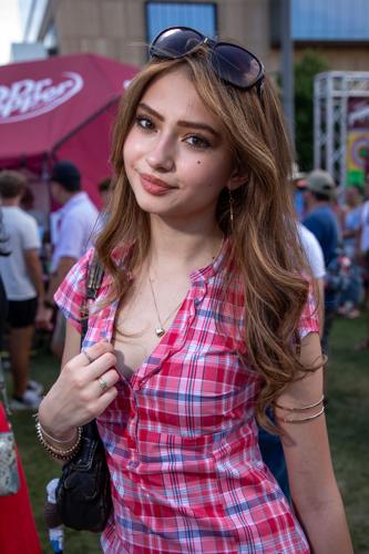 Color street style portrait of CMA Fest fan September Rose, sporting a plaid Y2K-inspired outfit with big sunglasses and a little purse.