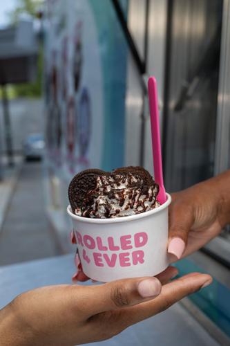 A hand passing a cup of ice cream topped with oreo cookies to a customer at Rolled 4 Ever